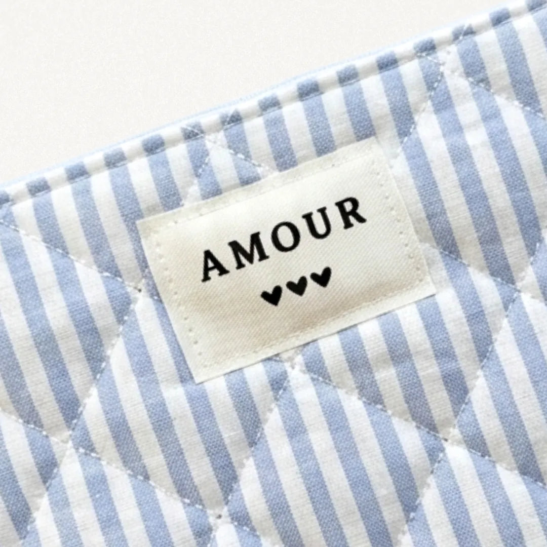 Pochette matelassée en tissu rayé blanc et bleu clair avec étiquette "AMOUR" et 3 cœurs noirs.