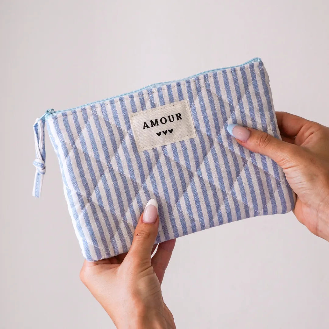 Pochette textile matelassée à rayures verticales blanches et bleues. Étiquette "AMOUR" et 3 cœurs noirs, tenue par deux