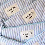 Trois pochettes en tissu matelassé à rayures bleues et blanches. Fermetures éclair bleues. Étiquettes "AMOUR" et trois cœurs