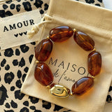Bracelet perles ambre et or présenté sur sa pochette en tissu beige Maison de l'Amour et trousse léopard.