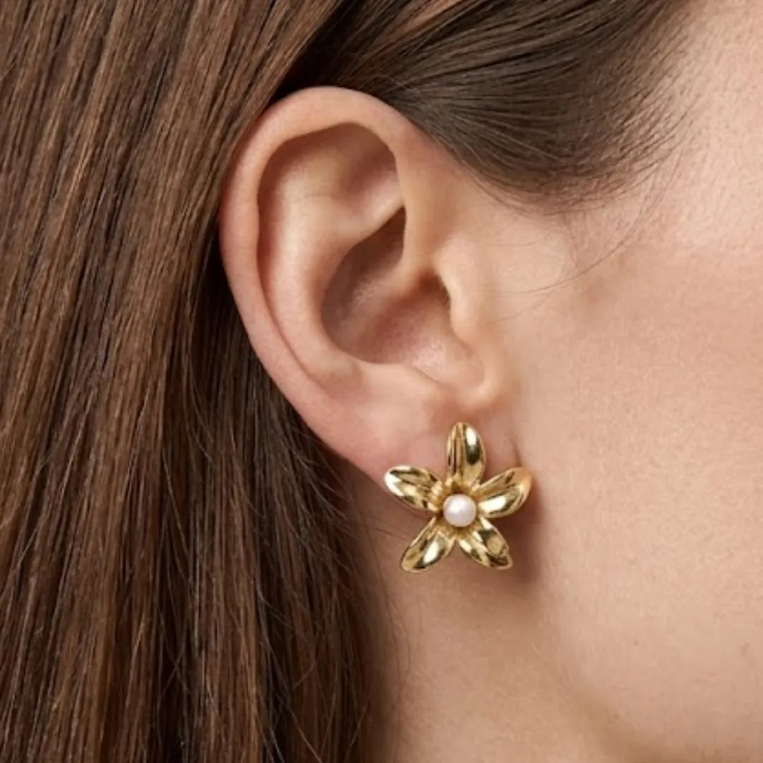 Boucle d'oreille puce fleur en acier inoxydable doré, avec une perle blanche au centre, portée sur une oreille.