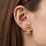 Boucle d'oreille puce fleur en acier inoxydable doré, avec une perle blanche au centre, portée sur une oreille.
