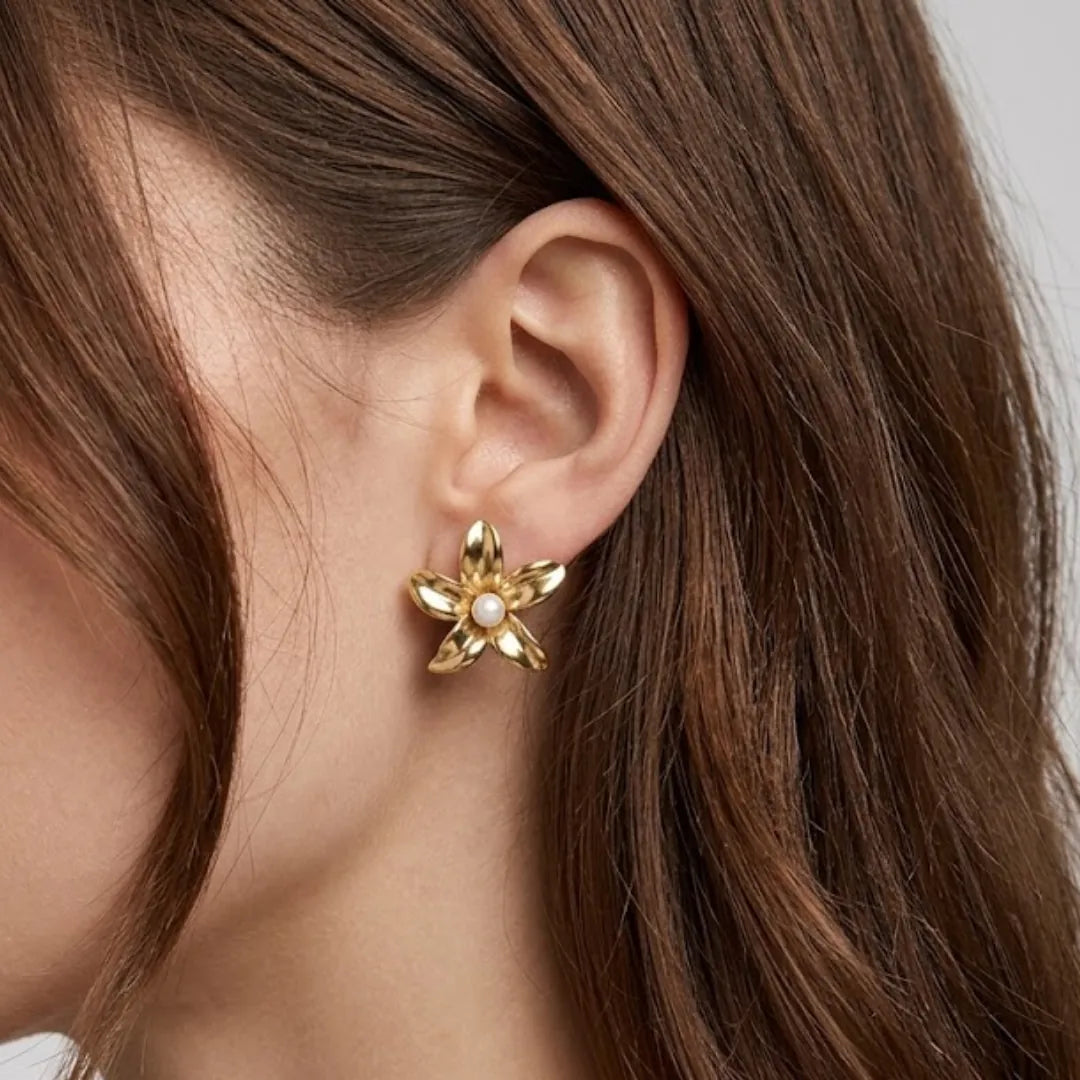 Puce d'oreille fleur en acier inoxydable doré avec perle blanche au centre, portée sur une oreille.
