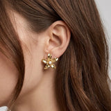 Puce d'oreille fleur en acier inoxydable doré avec perle blanche au centre, portée sur une oreille.