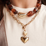 Femme portant une accumulation de bijoux MAISON DE L'AMOUR : bagues dorées, bracelets joncs et colliers superposés avec veste en cuir.