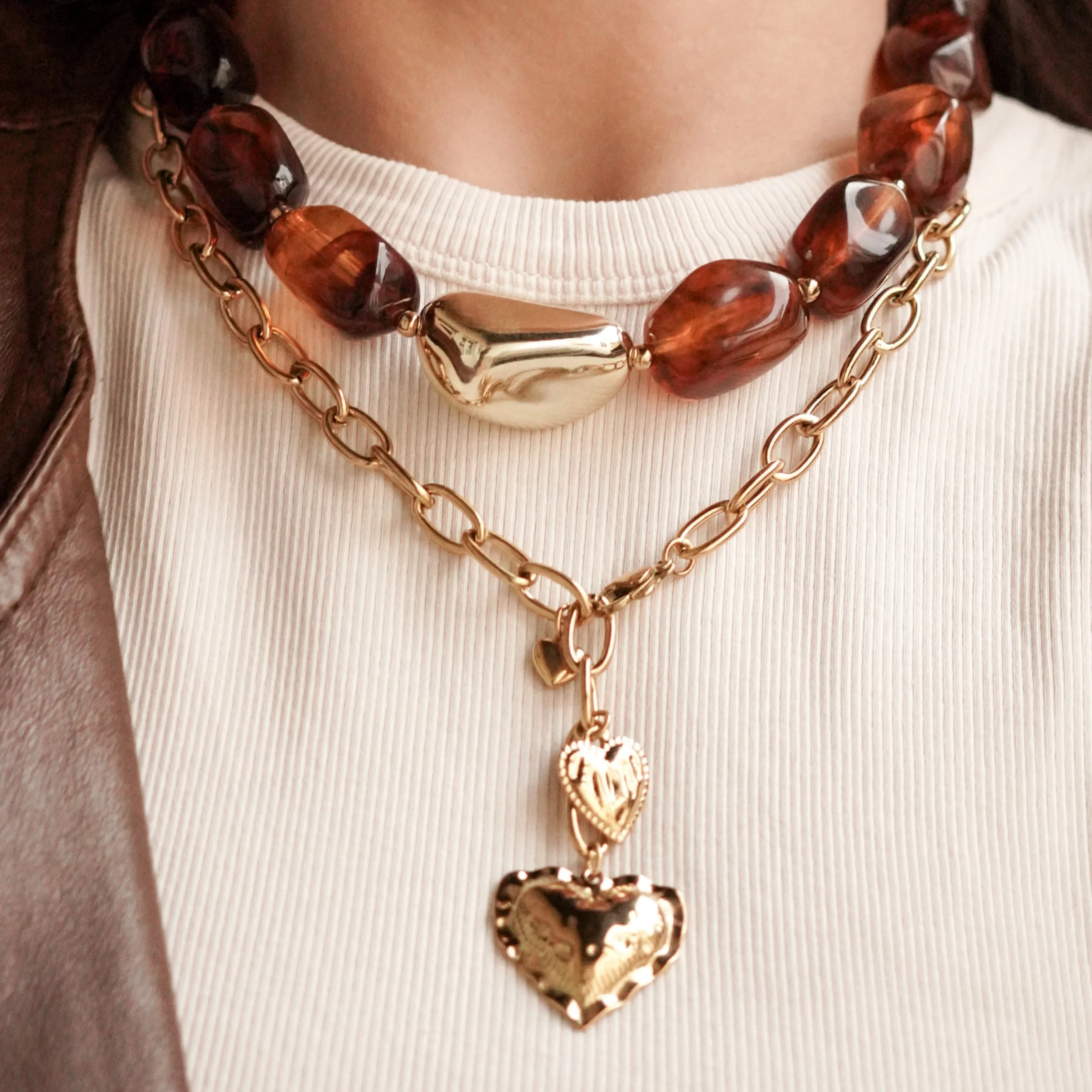 Femme portant une accumulation de bijoux MAISON DE L'AMOUR : bagues dorées, bracelets joncs et colliers superposés avec veste en cuir.