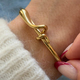 Bracelet jonc doré à nœud porté au poignet, associé à un pull en maille blanche douce pour un look hivernal.