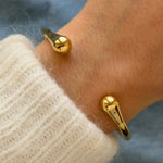 Bracelet jonc ouvert doré porté au poignet associé à un pull en maille blanche douce pour un style hivernal.