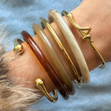 Accumulation tendance de bijoux au poignet : mélange d'un bracelet jonc doré à nœud et de joncs en résine colorée.