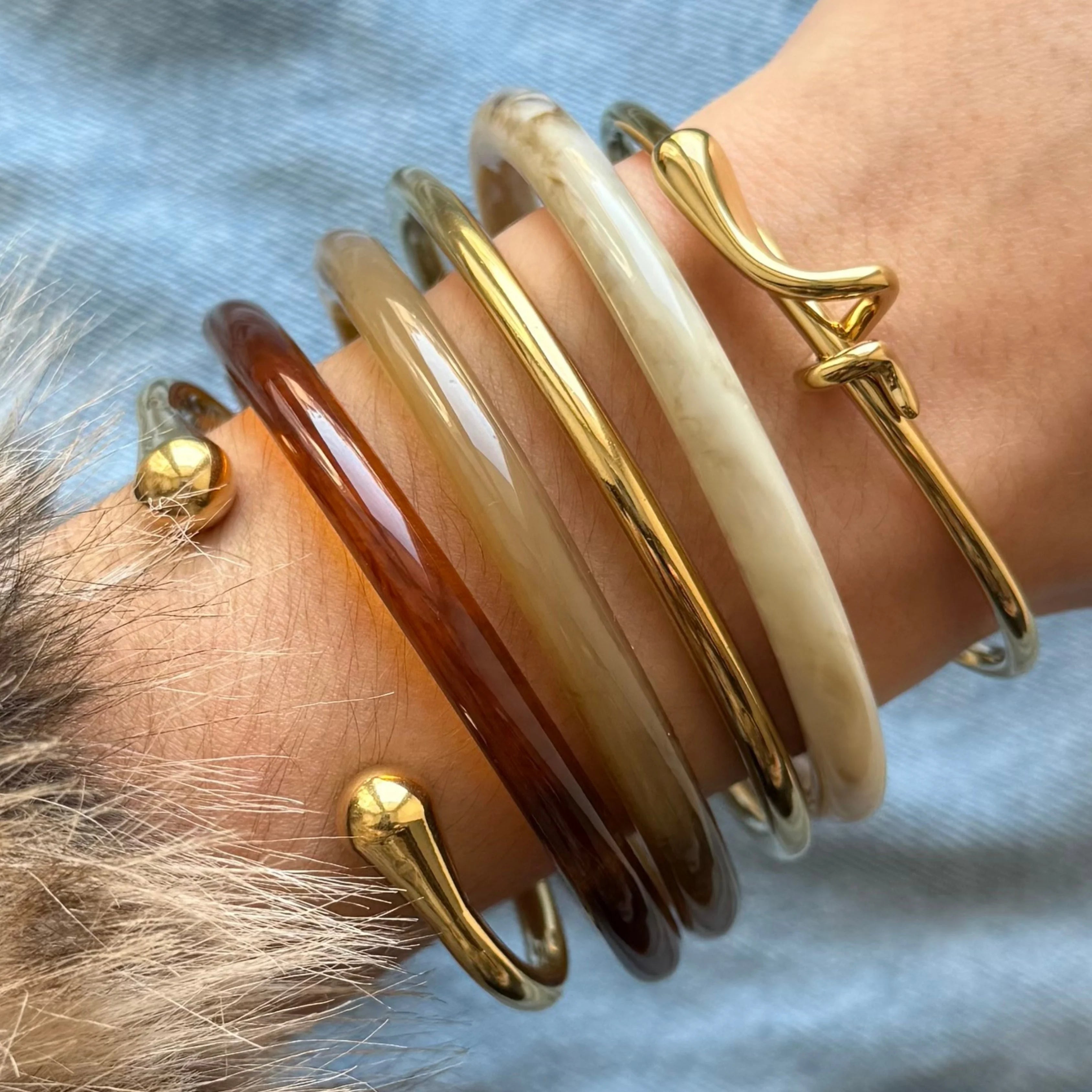 Accumulation tendance de bijoux au poignet : mélange d'un bracelet jonc doré à nœud et de joncs en résine colorée.