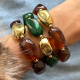 Accumulation de trois bracelets élastiques composés de grosses perles irrégulières en résine verte, marron effet écaille et dorée brillante.