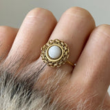 Détail d'une bague style bohème avec pierre blanche et contour chaîne dorée portée au doigt.