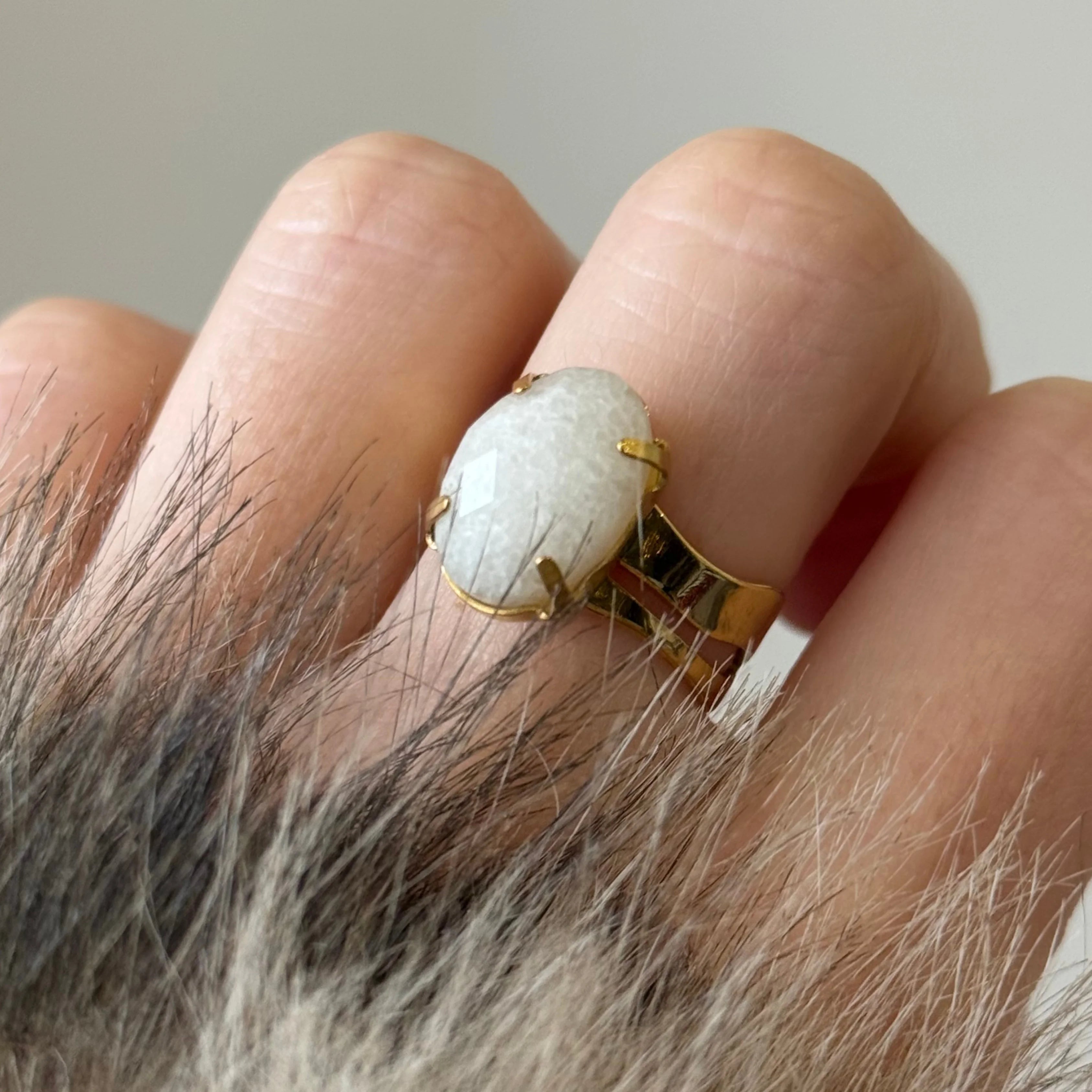Détail d'une bague avec pierre blanche texturée portée au doigt, mettant en avant le sertissage à griffes dorées.