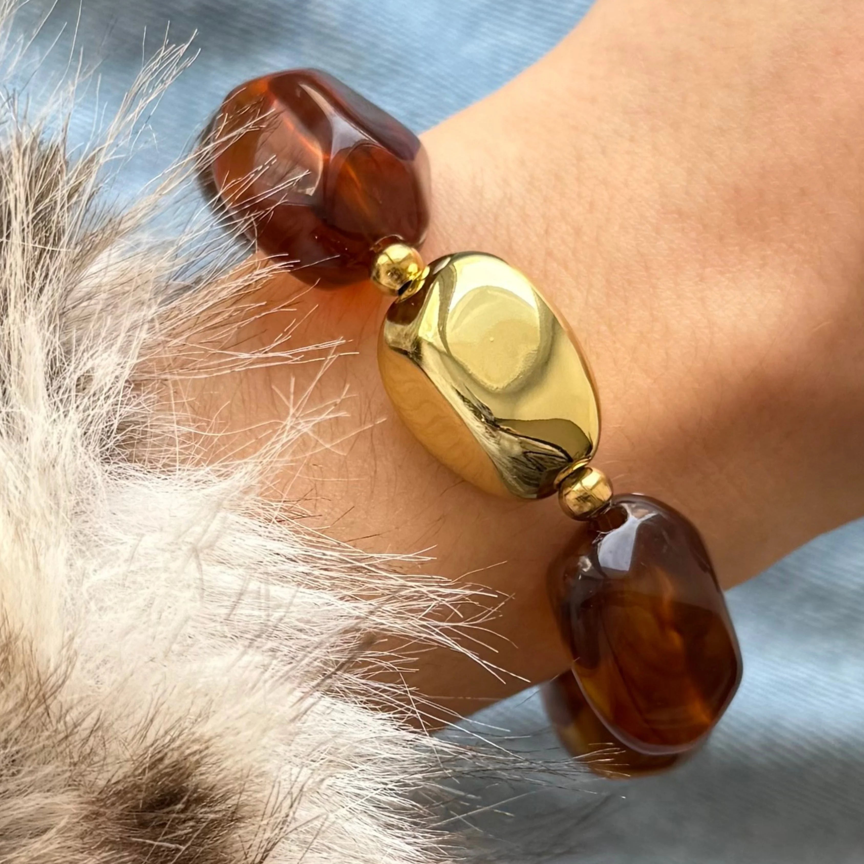 Gros plan sur un bracelet porté au poignet montrant la texture des perles effet écaille de tortue et le détail doré.