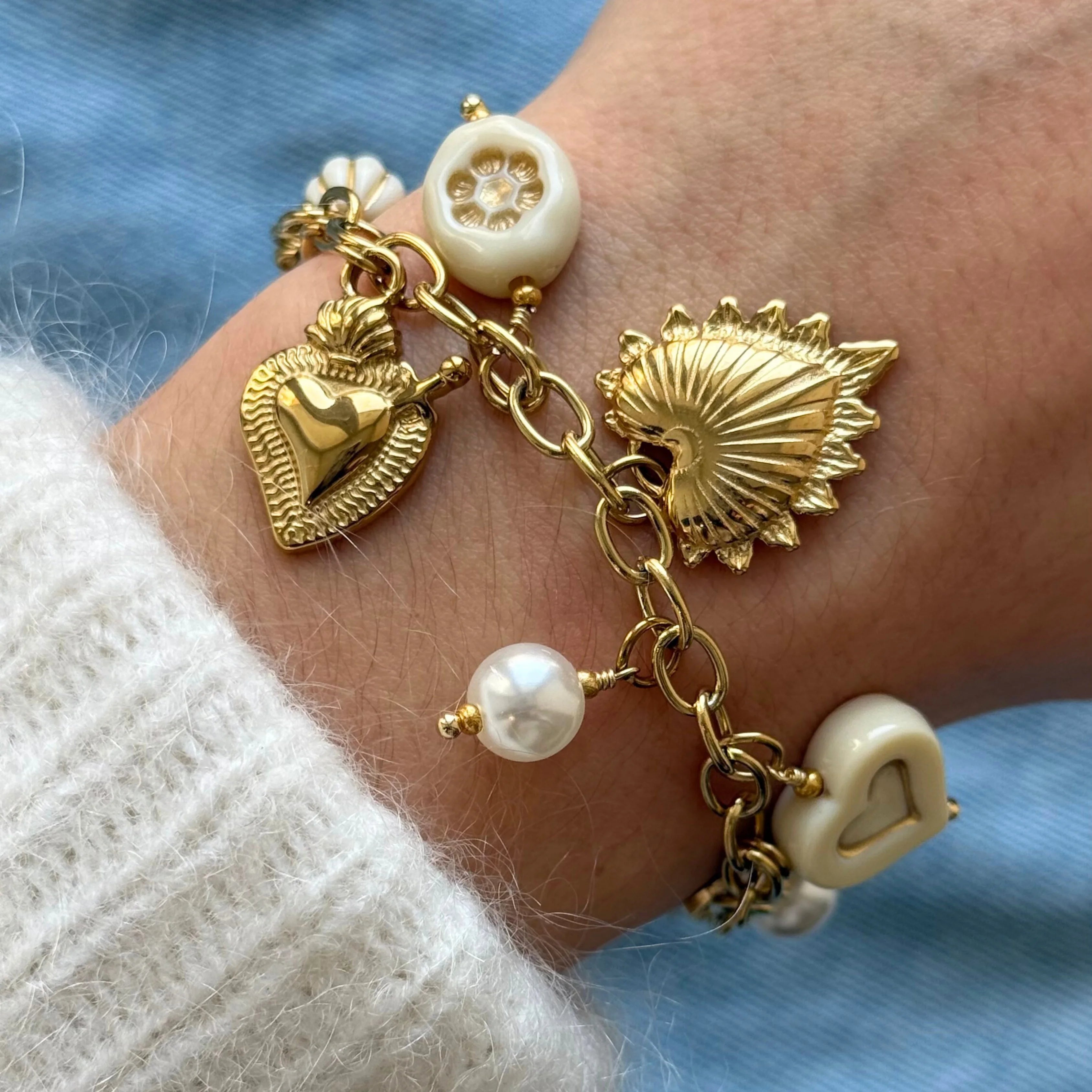 Gros plan sur les détails du bracelet porté : breloque cœur sacré rayonnant doré et perles fantaisie blanches.